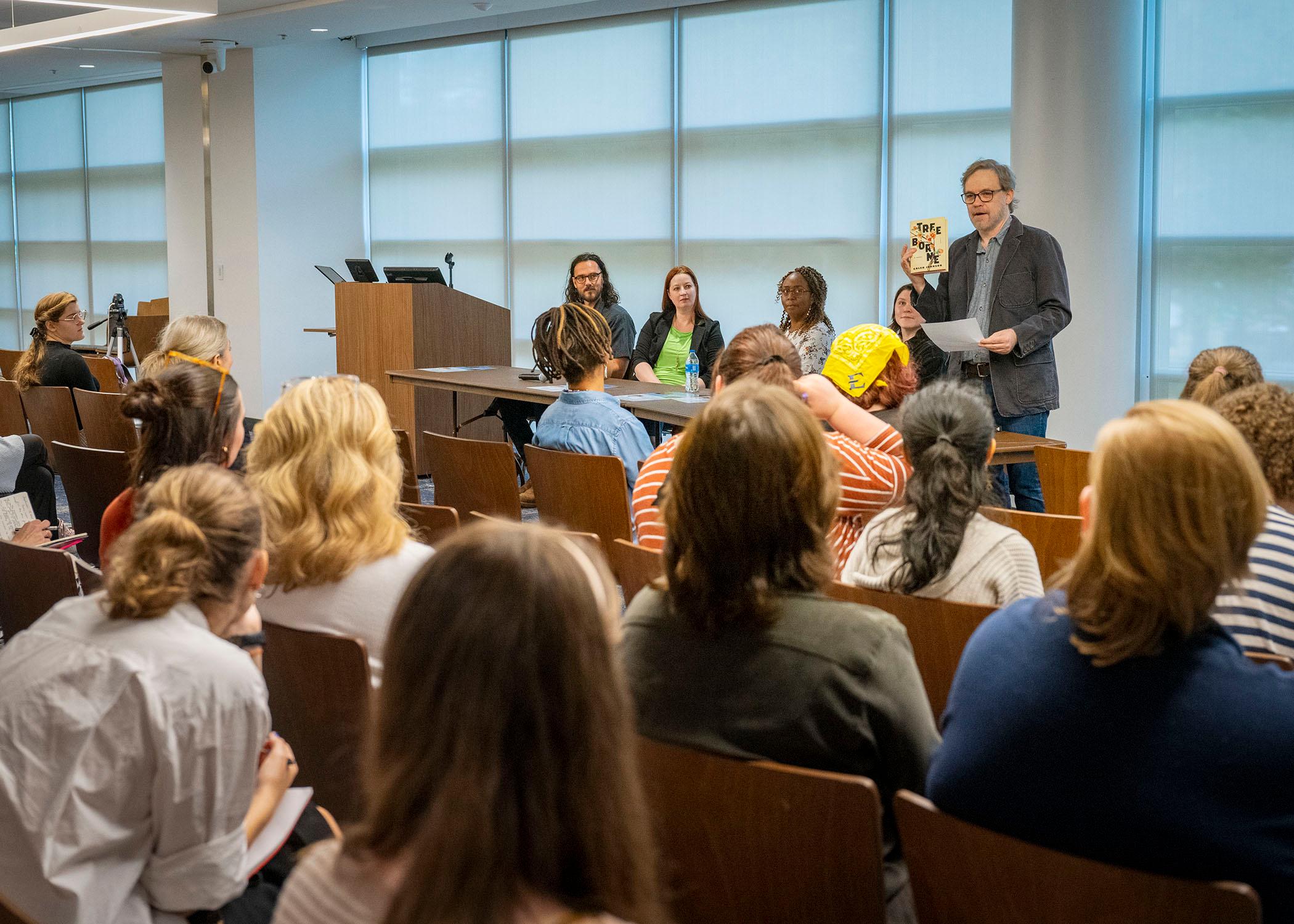 Dr. Jesse Graves introduces the Three Emerging Writers panel, holding up Caleb Johnson's novel, Tree Borne.