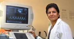 Department of Biomedical Sciences Chair, Dr. Krishna Singh pictured in her white lab coat beside a computer machine.