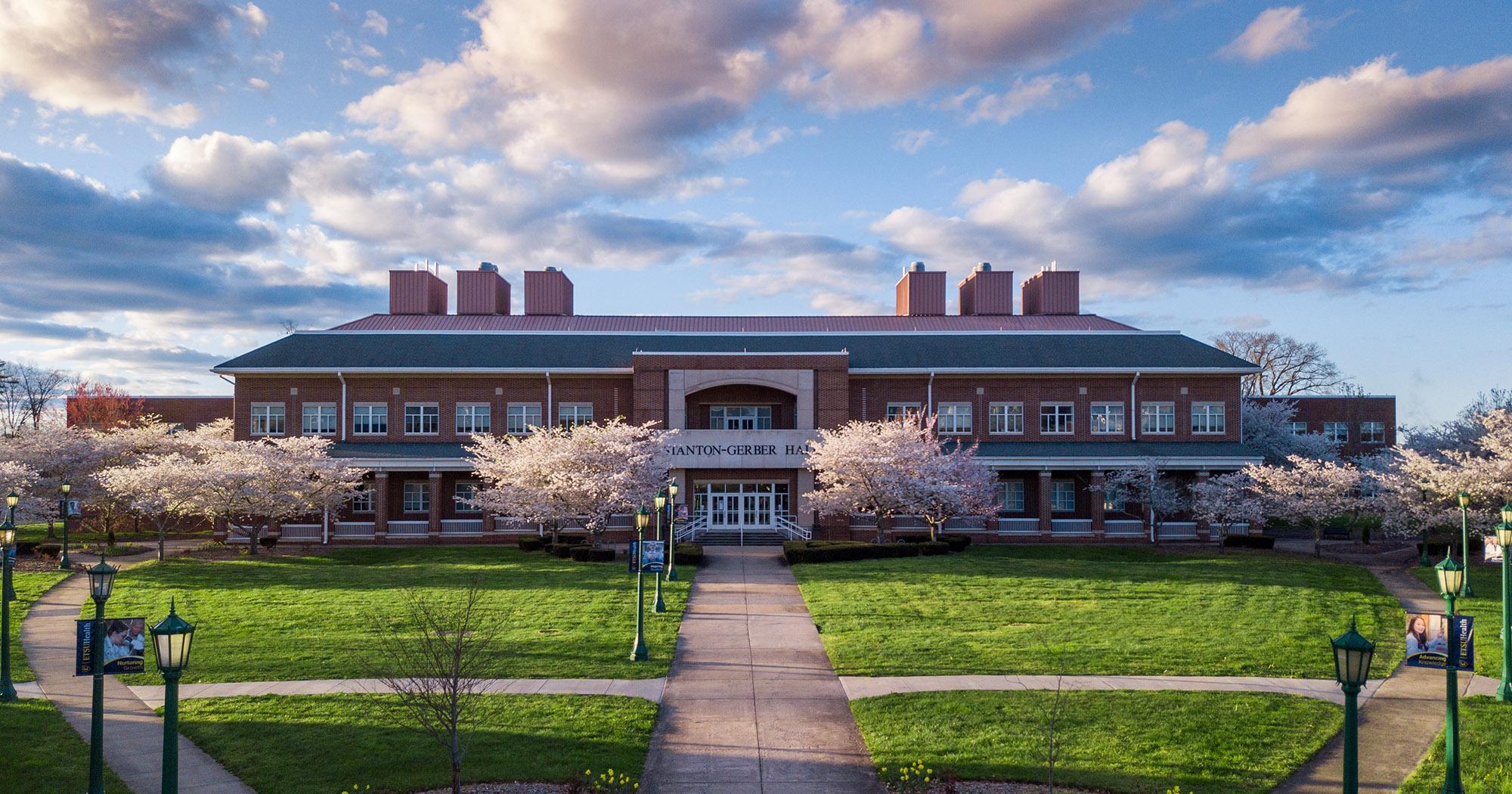 A front view of Stnaton-Gerber Hall with a cloudy blue sky, and cherry blossom trees in bloom.