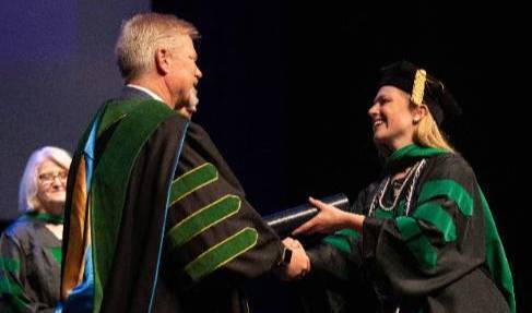 The dean of Quillen College of Medicine handing a diploma to a graduated medical students, and shaking hands. They are all wearing regalia attire.
