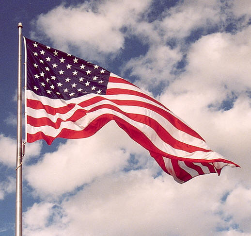 American flag on its flagpole waving in the wind with a cloudy sky in the background