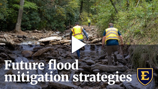 YouTube thumbnail depicting two workers in vests traverse across a creek in a rocky forest setting.